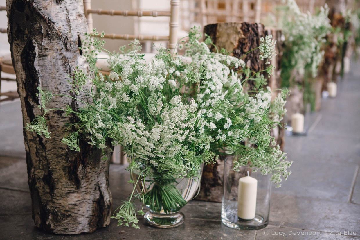 White flowers in a glass vase next to a candle in a glass vase