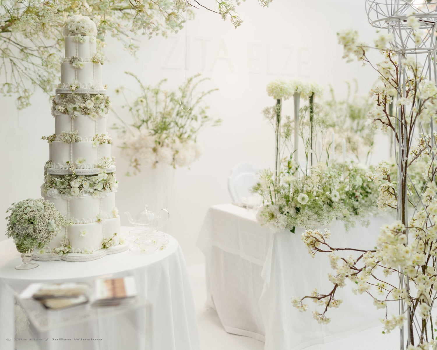 All white wedding setting with wedding cake and flower arrangement
