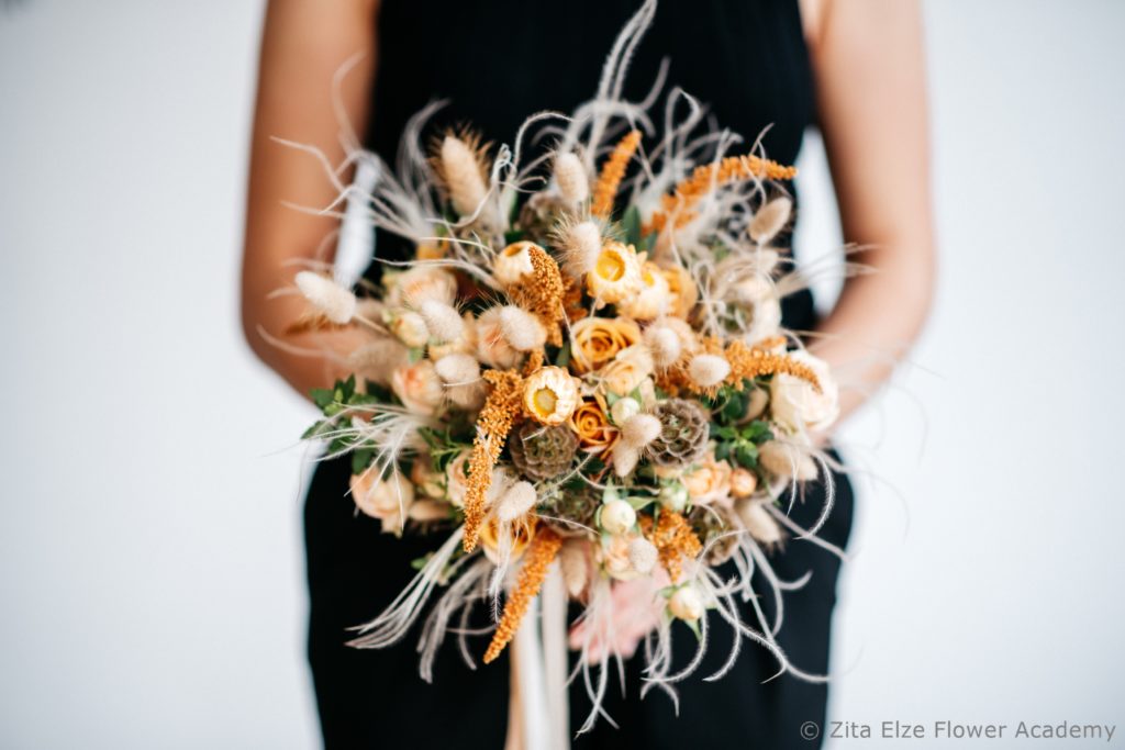 woman's arm holding an orange and blush dried flower bouquet 