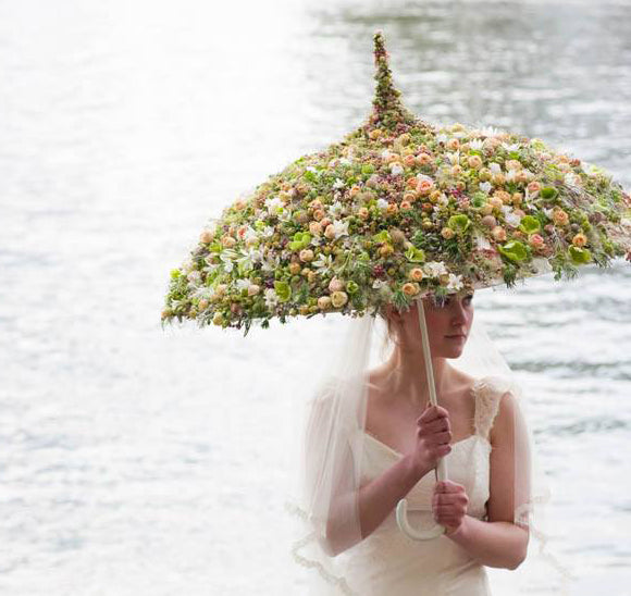 bride holding an umbrealla coated with flowers nd water in the background