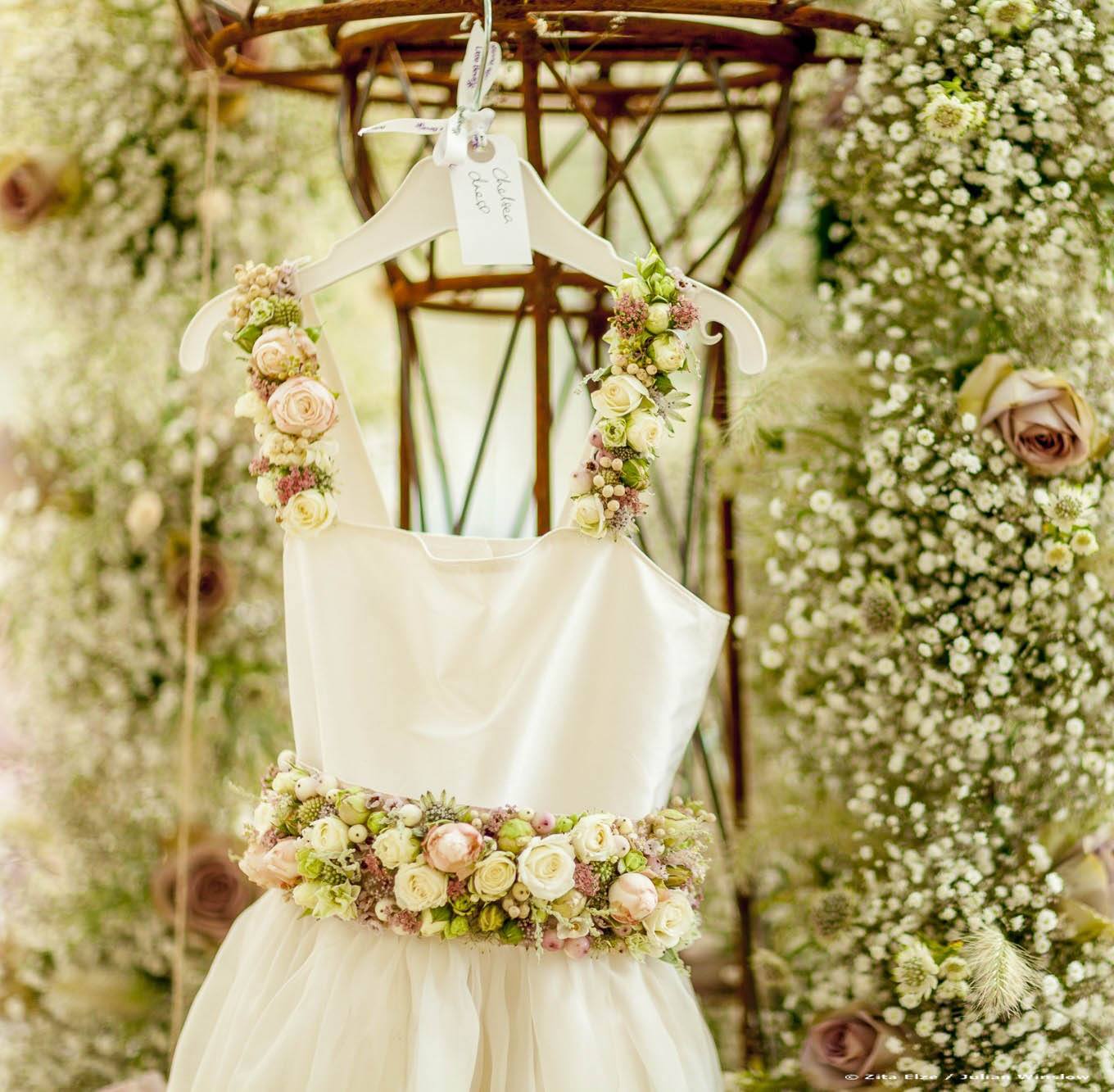 detail of a white dress with a belt and shoulder straps made with flowers and flowers in the background